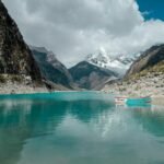 Stunning turquoise lake surrounded by mountains in Huaraz, Peru on a crisp day with a lonely boat.